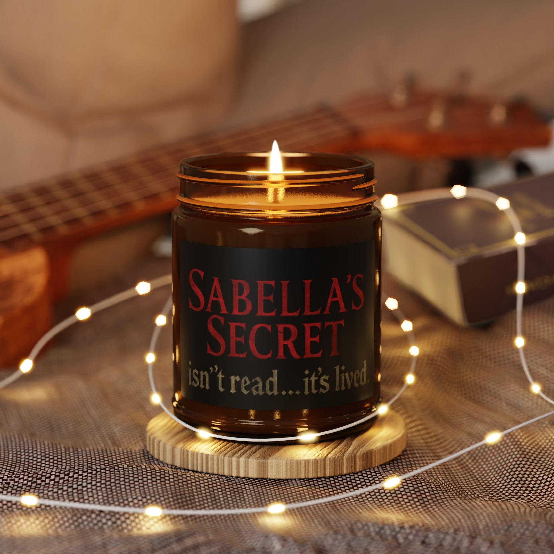 Candle in a jar labeled 'Sabella's Secret' with a guitar and string lights in the background