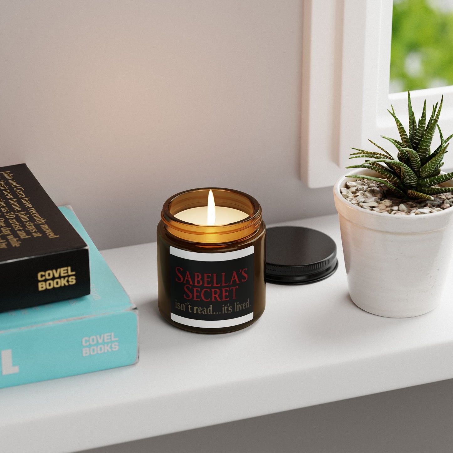 Candle labeled 'Sabella's Secret' on a shelf with books and a plant