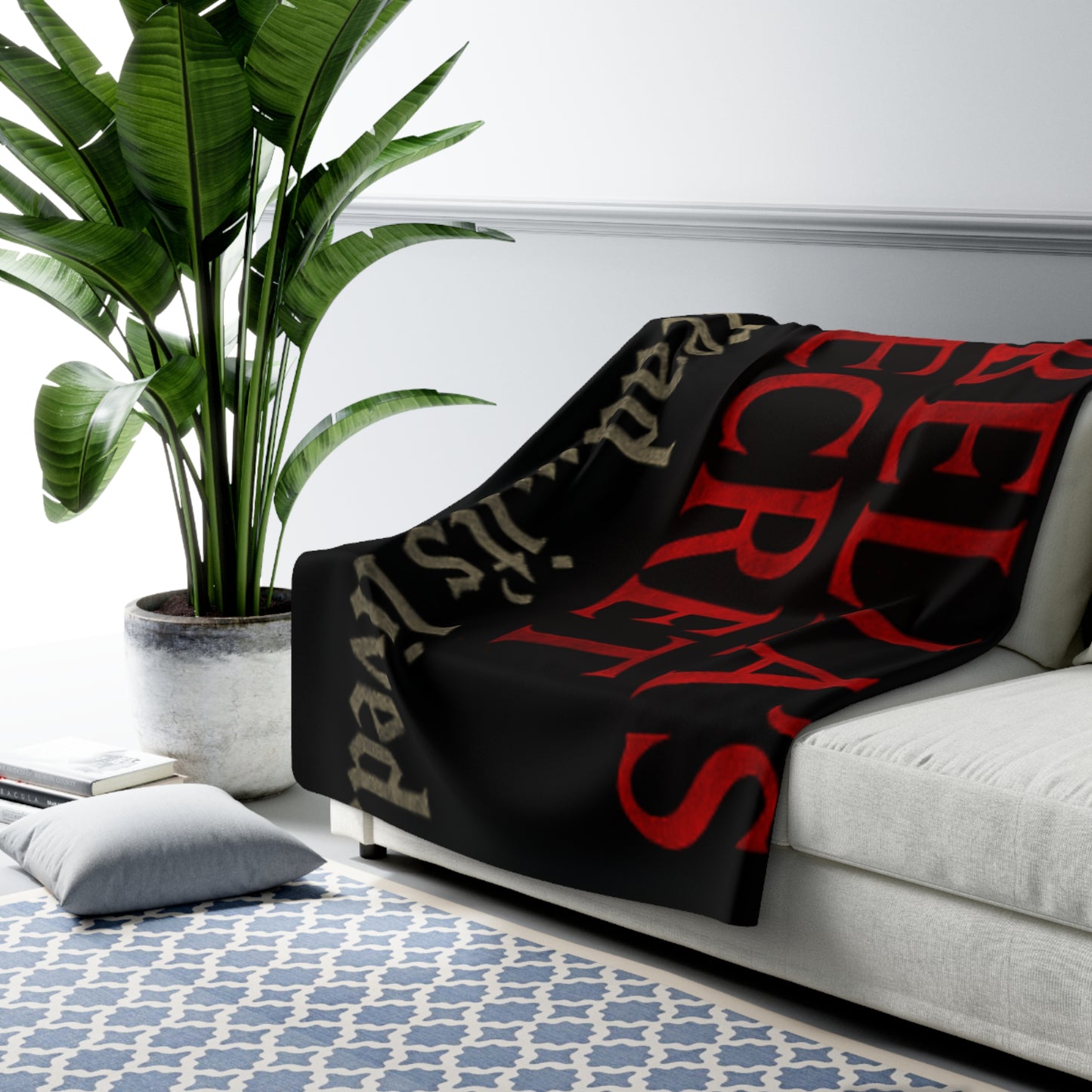 Black blanket with red and beige text draped over a couch in a living room setting.