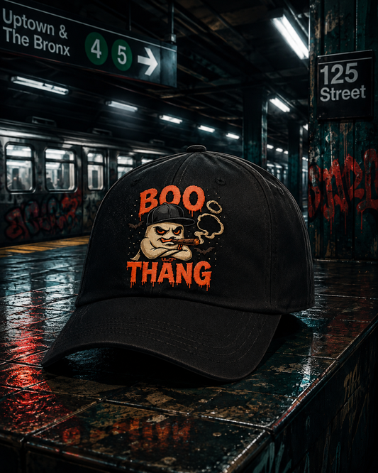 Boo Bastic black embroidered dad cap resting on NYC subway platform bench at 125th Street, Boo Thang ghost character design in orange on front panel