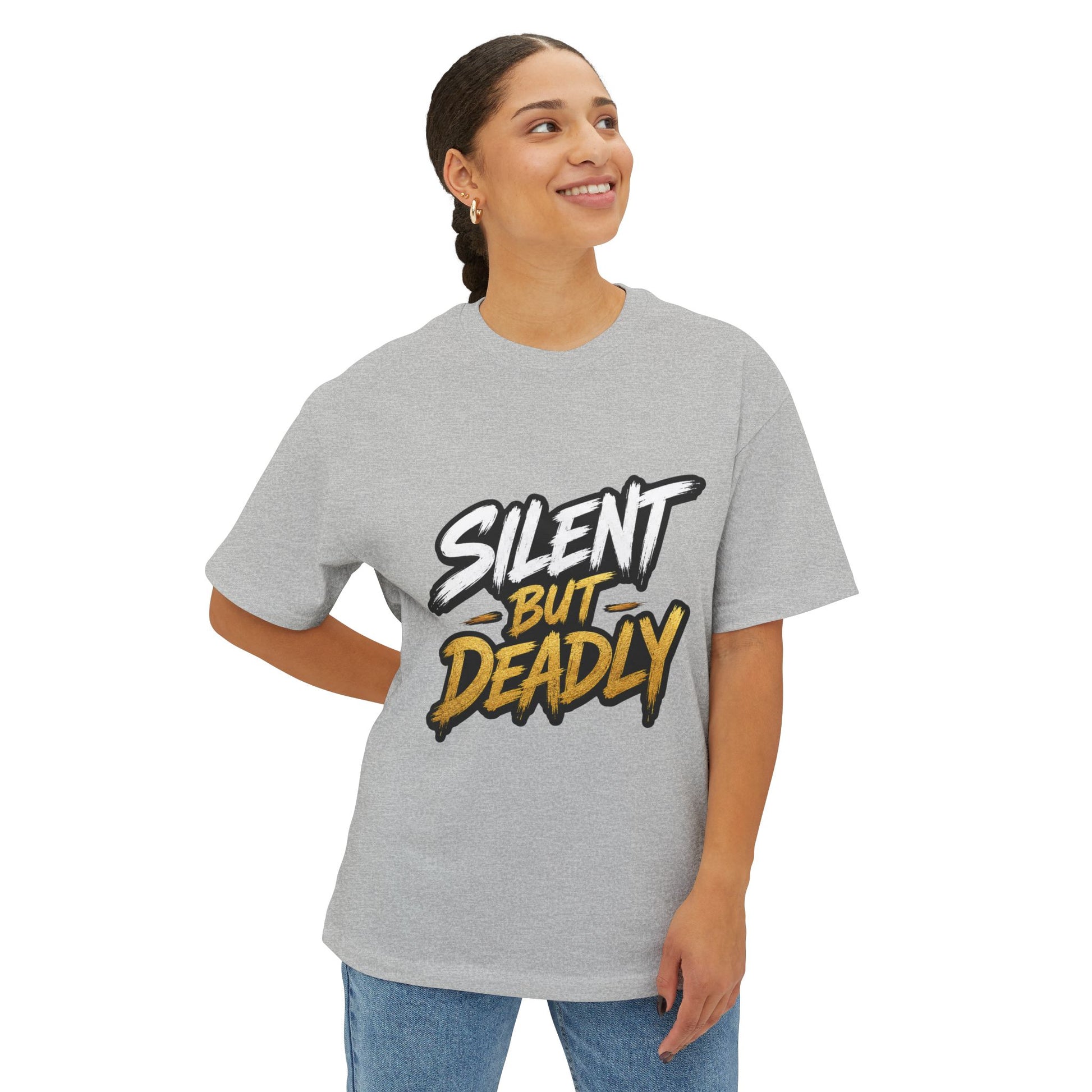 A woman wearing a light heather gray t-shirt with a graphic that reads 'SILENT BUT DEADLY' in stylized white and yellow lettering with black outlines, paired with blue jeans, against a plain white background.