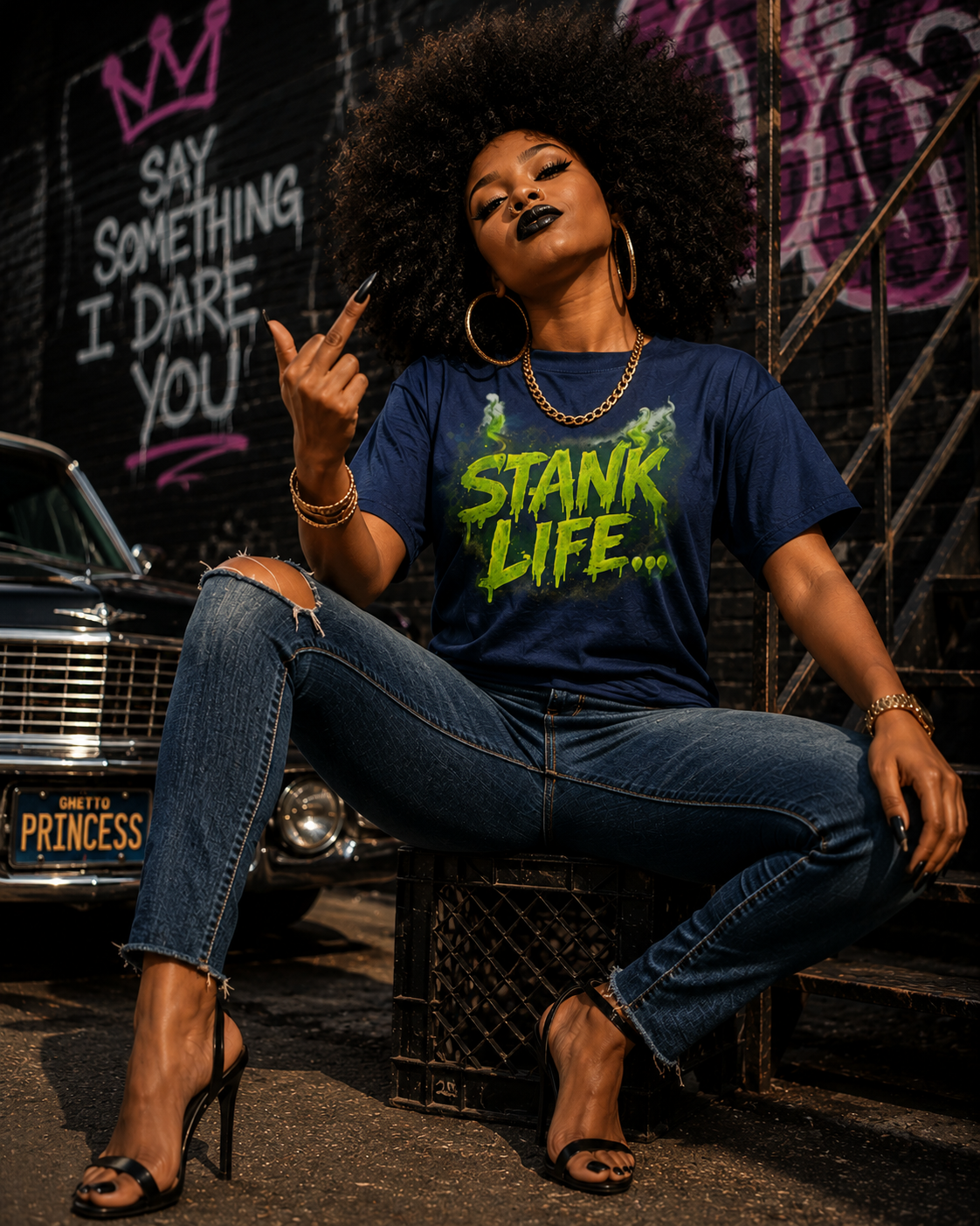 "Stank Life graphic tee in navy blue — bold neon green drip text worn by woman with natural afro, seated against urban graffiti backdrop"