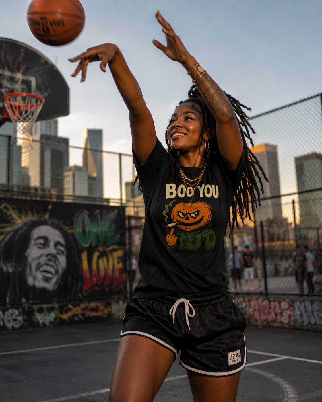 Black (woman, basketball court, city skyline, Bob Marley mural) — "Woman in black Boo You Stank Statement Tee shooting a basketball on an outdoor court with a city skyline and Bob Marley mural in the background, street style"