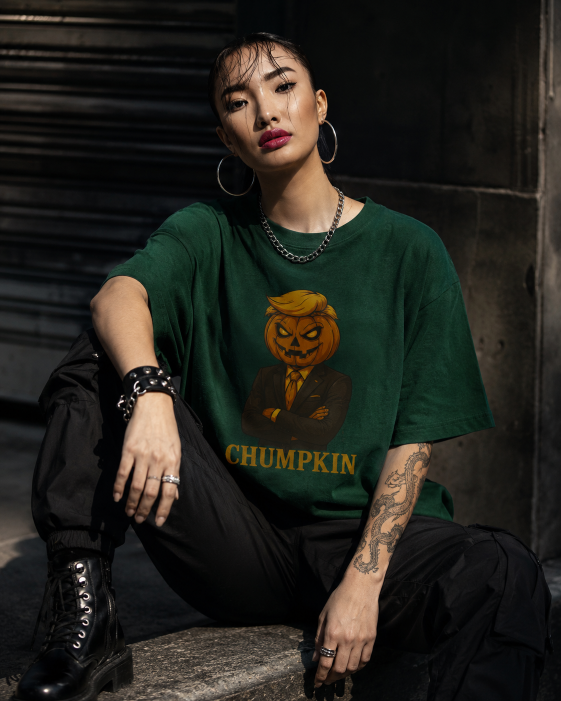 Forest Green (woman, dark alley, chain necklace, tattoo sleeve) — "Woman in forest green Chumpkin Boo Thang graphic tee seated in a dark urban alley with chain necklace and dragon tattoo sleeve, edgy street style"